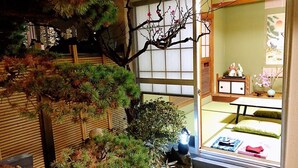 Ein traditioneller japanischer Raum mit Tatami-Boden, einer Shoji-Schiebetür und einem kleinen Garten mit Bonsai-Bäumen und einem Stein Laternen.