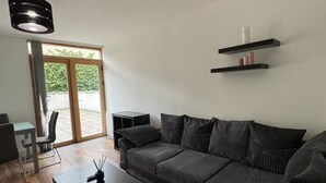 A modern living room with a sectional sofa, a coffee table, and a TV stand. There is a sliding glass door leading to an outdoor area.