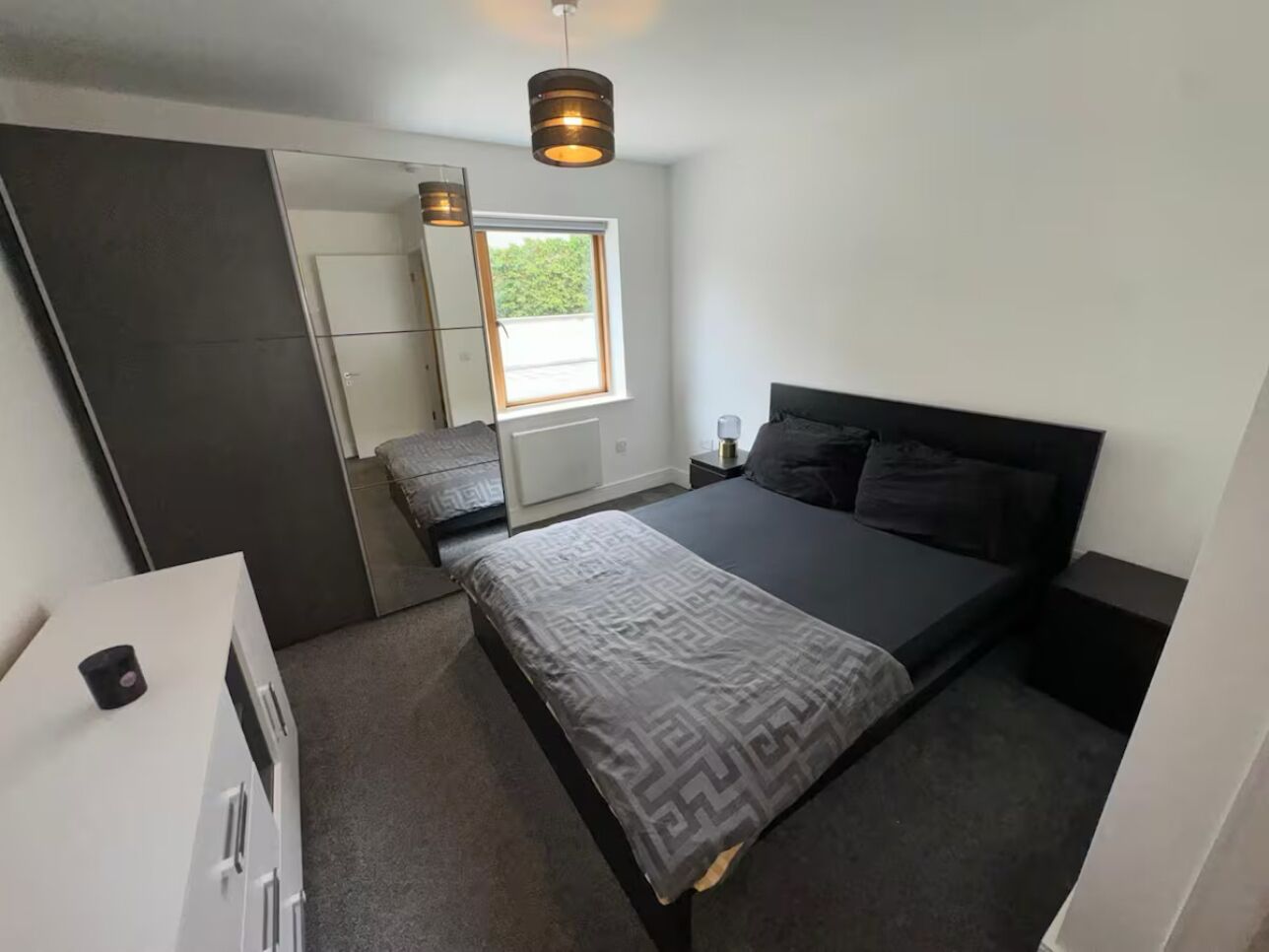 Un dormitorio moderno con una cama, mesitas de noche, un aparador, una ventana y un espejo.
