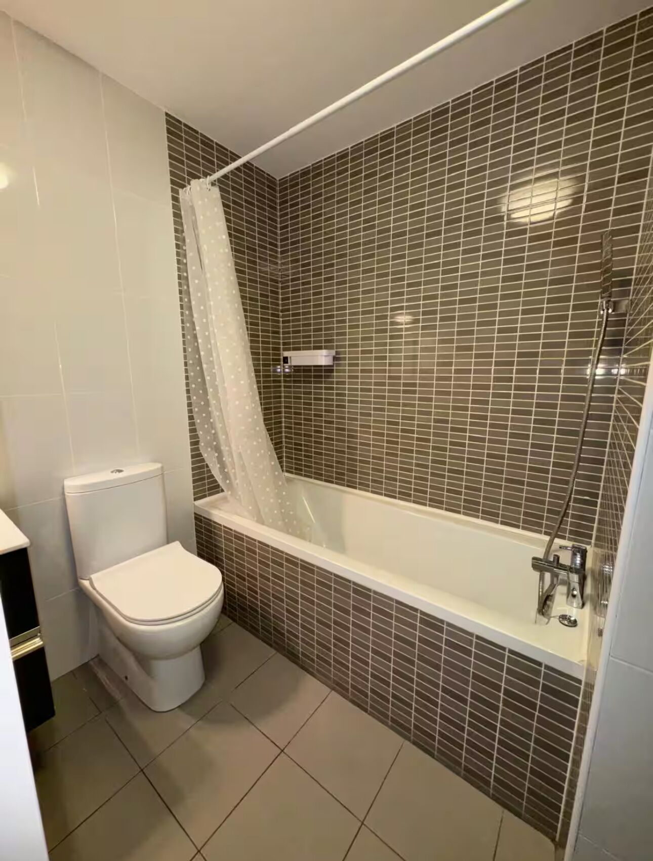 A bathroom with a toilet, a shower with a glass enclosure, and tiled walls.