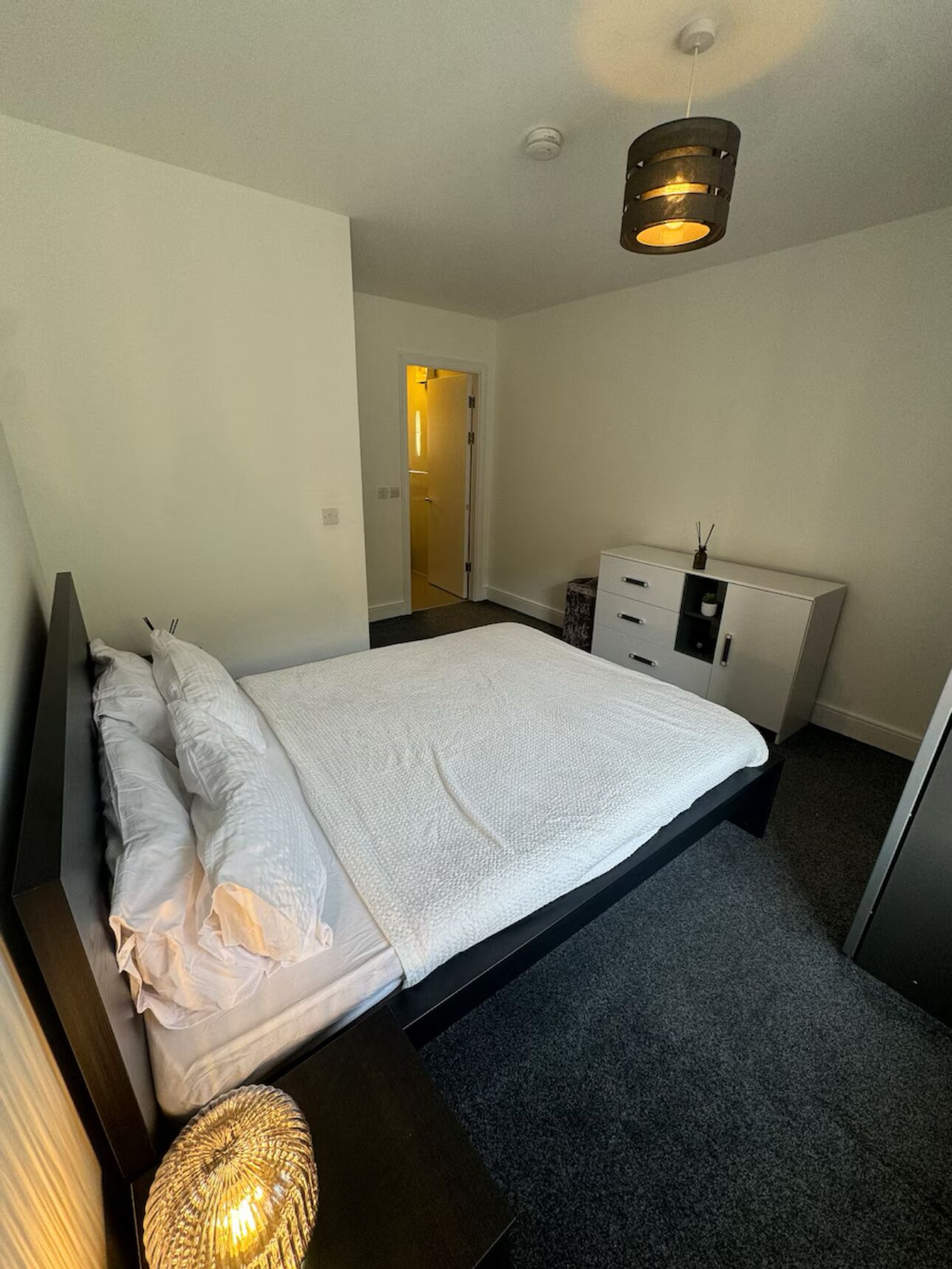 Un dormitorio moderno con una cama grande, una mesita de noche, un aparador y una lámpara colgante.