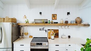 A kitchen with a stainless steel refrigerator, a stove, and a wooden countertop. There are shelves above the counter holding various kitchen items and a hanging light fixture. - Walk to the Beach! Boho-Inspired 2BR Jupiter Loft w Private Outdoor Space (Jupiter)
