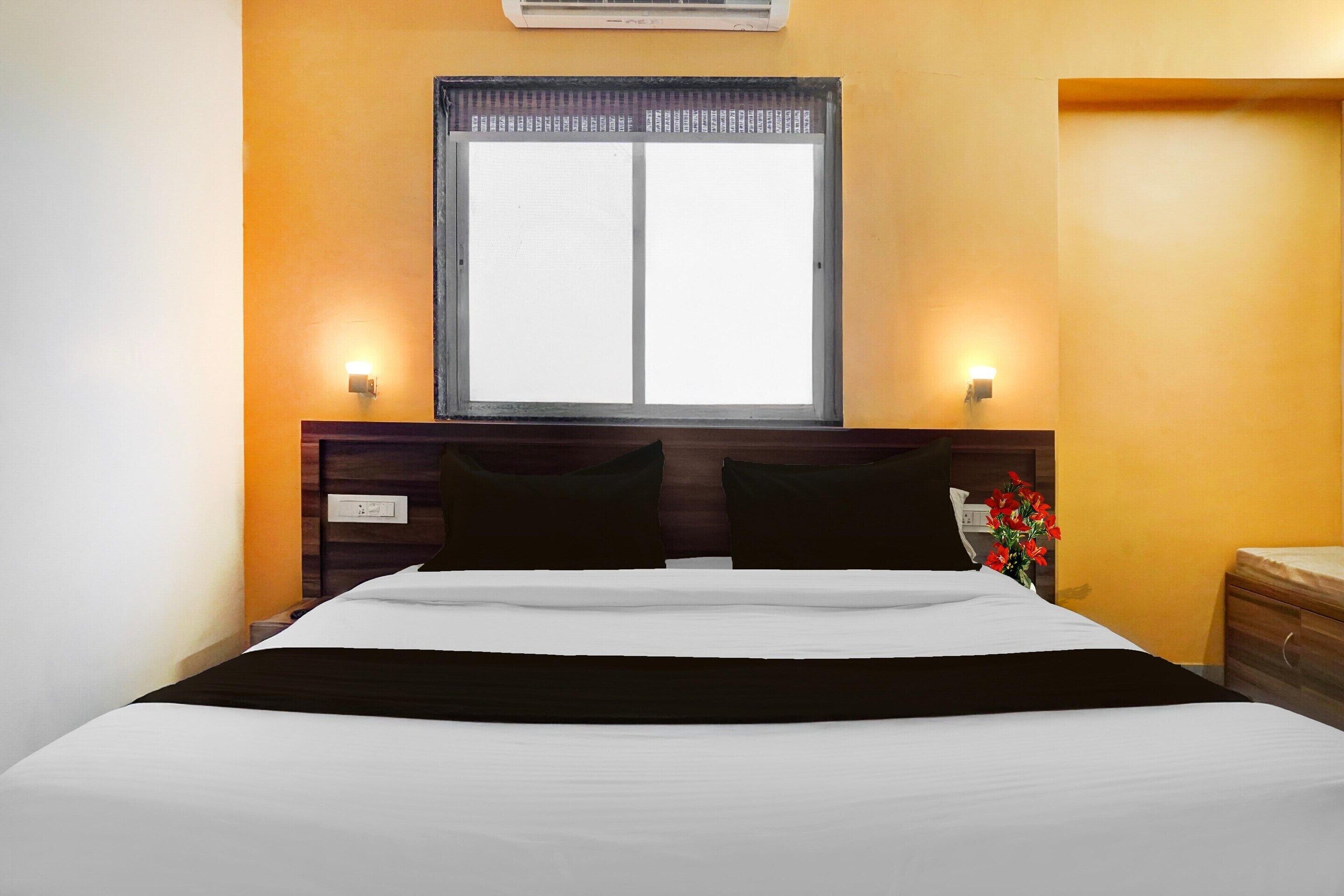 A hotel room with a bed, a window, a nightstand, and a wall-mounted air conditioner.