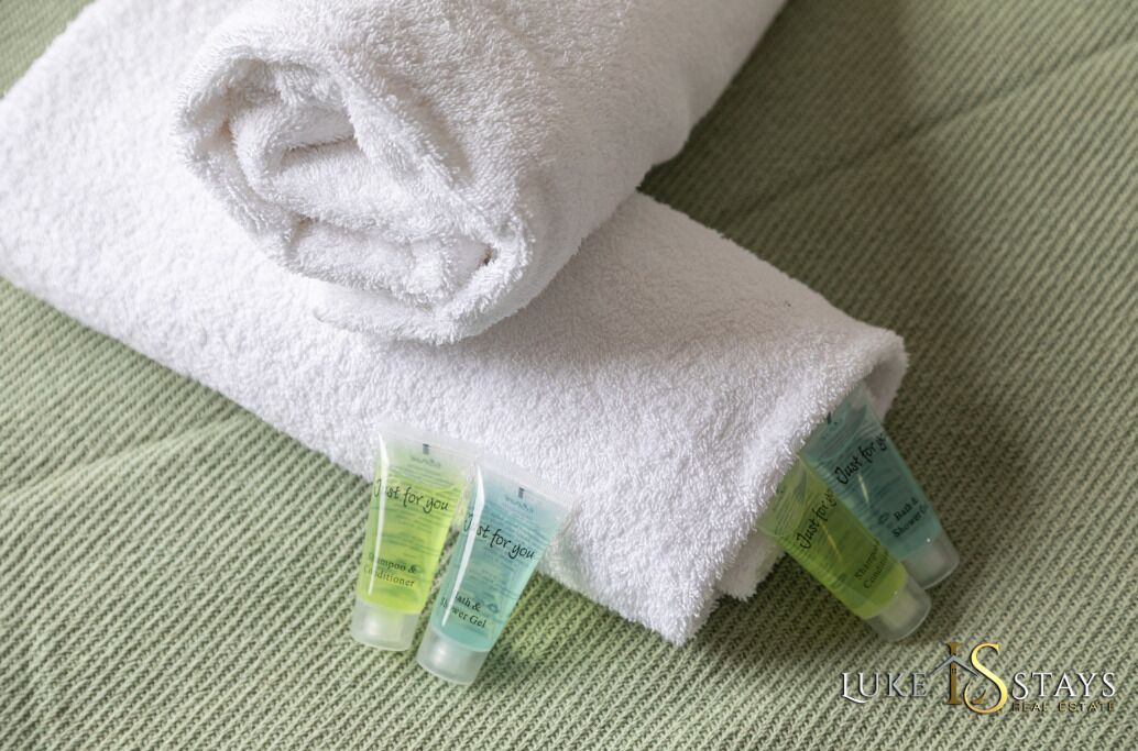 A neatly folded white towel on a textured green surface, accompanied by two tubes of lotion.