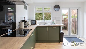 A modern kitchen with a central island, a built-in oven, and a microwave. There is a window with a view of greenery outside.