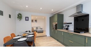 A modern kitchen with green cabinets, a black stove, and a dining area with a table set for four. - Luke Stays - Lonnen Drive (Swalwell)