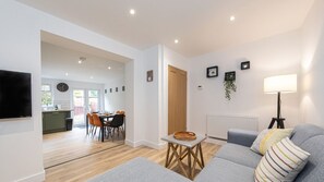 A modern living room with a grey sofa, a dining area with a table and chairs, and a kitchen in the background. - Luke Stays - Lonnen Drive (Swalwell)
