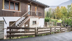 A two-story wooden house with a stone base, a wooden staircase, and a balcony.