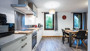 A modern kitchen with a stove, oven, and microwave, a dining table with chairs, and a window with a view of greenery.