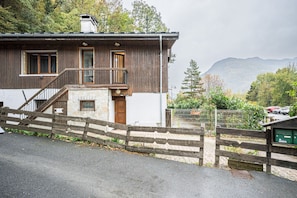 A wooden house with a balcony, a staircase, and a view of mountains.