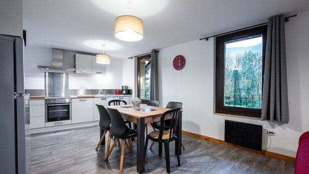 A modern kitchen with a dining area, large windows with a view, and a clock on the wall.