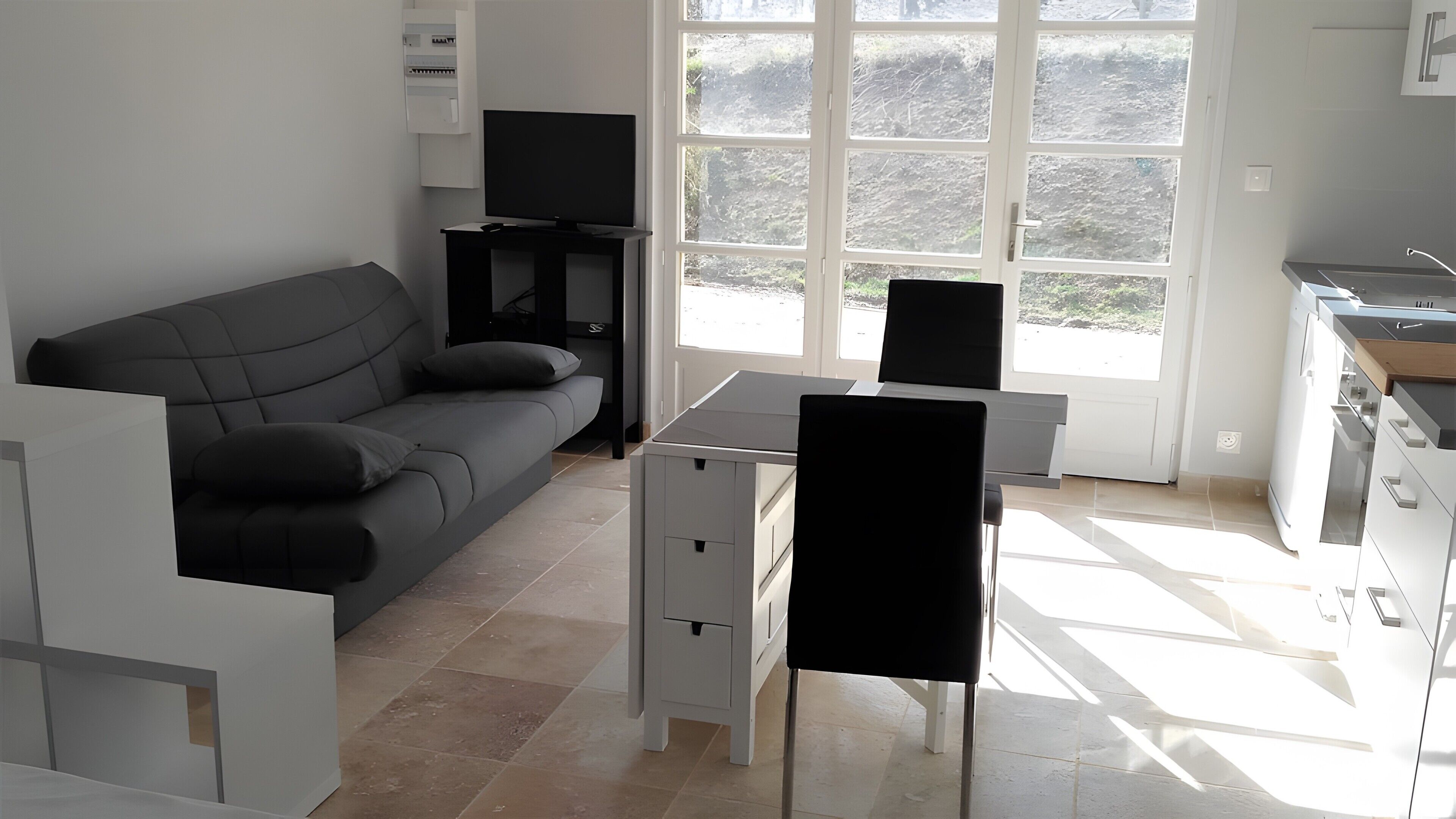 Ein modernes Wohnzimmer mit Sofa, Fernseher, Esstisch und Küchenzeile mit Fenster.