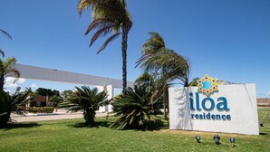 Señal de Ilôa Residence con una vista despejada del entorno, incluyendo palmeras y un edificio al fondo.