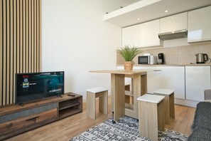 Une cuisine moderne avec une table en bois, des meubles blancs et un téléviseur diffusant un film.