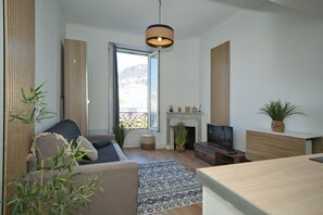 Un salon moderne avec un canapé, un téléviseur, une cheminée et une grande fenêtre.