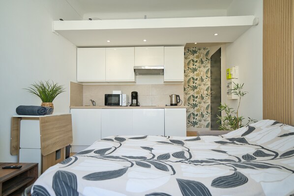 A compact hotel room with a bed, a small kitchenette, and a bathroom.