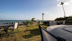 Un área de estar al aire libre con mesas y sillas, vista al océano y una palmera.