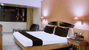A hotel room with a large bed, bedside tables, a desk, and a chair. - Suite JM Road Krishna Presidency (Pune)