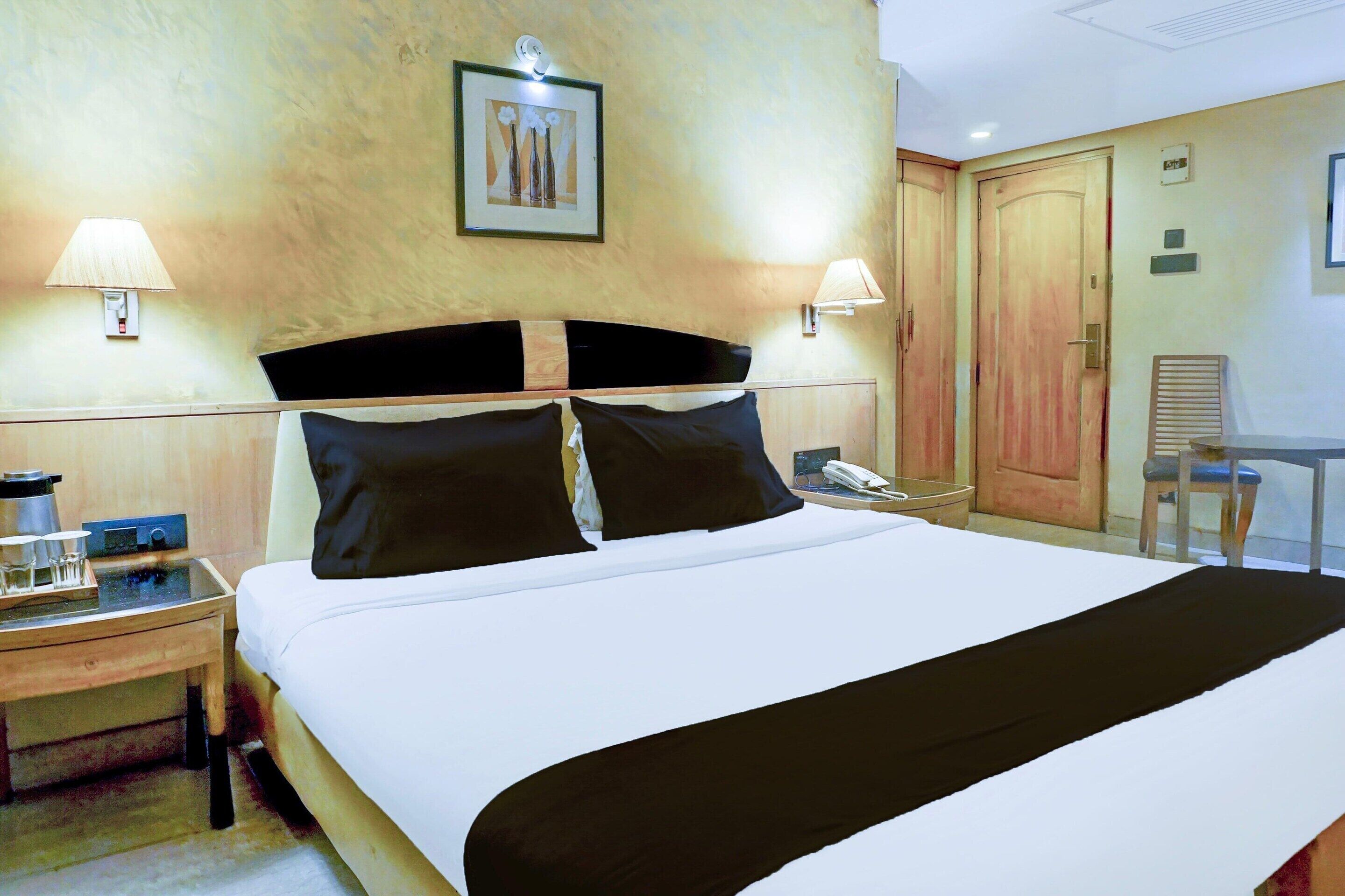Una habitación de hotel con cama, mesita de noche, lámpara y un cuadro en la pared.