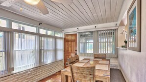 A dining area with a wooden table and chairs, large windows with blinds, a ceiling fan, and a door leading outside. - Coquina Hideaway (St. Pete Beach)