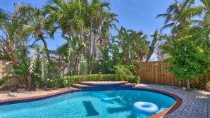 A swimming pool with a tiled edge, surrounded by palm trees and a wooden fence. - Coquina Hideaway (St. Pete Beach)