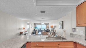 A modern kitchen with granite countertops, wooden cabinets, and a view to the living area. - Ram Sea I 405 (North Redington Beach)