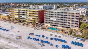 A beachfront hotel with multiple floors, a swimming pool, and a sandy beach with sun loungers. - Ram Sea I 405 (North Redington Beach)