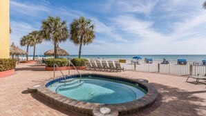 A swimming pool with a brick border, surrounded by lounge chairs and palm trees, with a view of the ocean. - Ram Sea I 405 (North Redington Beach)