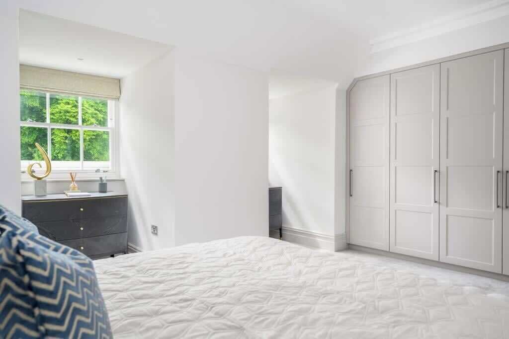 A bedroom with a bed, a dresser, a wardrobe, and a window with a view of trees.