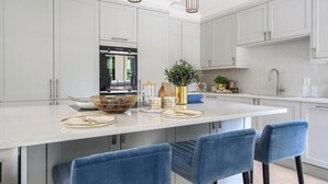 A modern kitchen with a large island, white cabinetry, and blue bar stools.