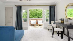 A room with a blue sofa, a desk with a chair, and a large window with curtains.