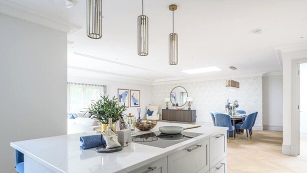 A modern kitchen with a large island, pendant lighting, and a dining area with blue chairs.