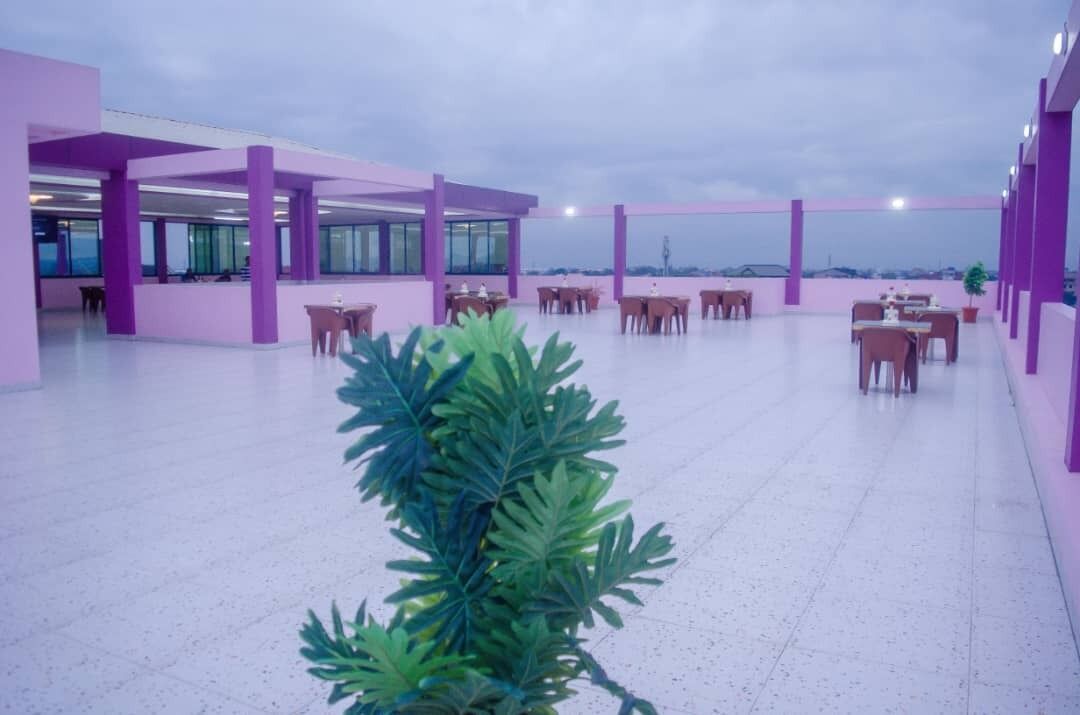 Un vaste espace extérieur agrémenté de piliers et de tables violets, avec une grande plante en premier plan.