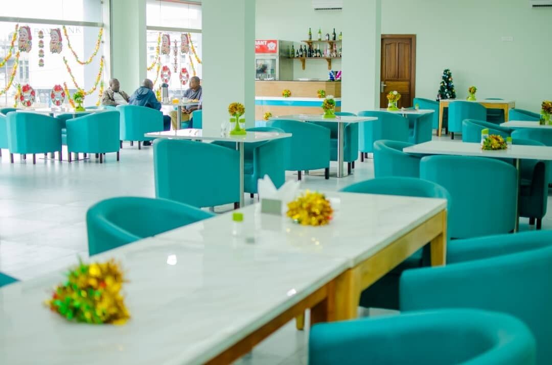A restaurant with teal chairs and white tables, decorated with yellow flowers.