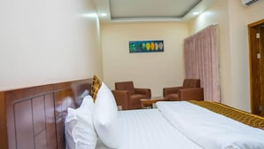 Een hotelkamer met een bed, twee bruine fauteuils, een tafeltje en een schilderij aan de muur.