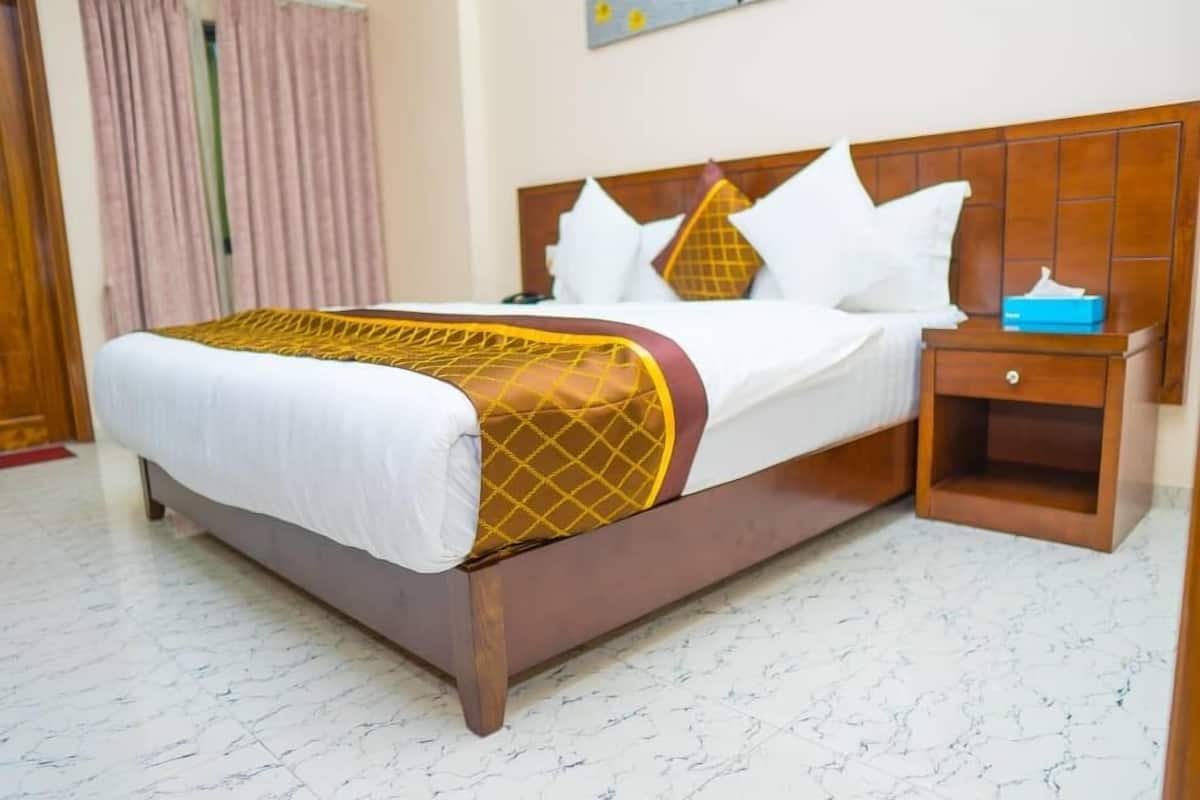Una cama con cabecera de madera, ropa de cama blanca y un detalle en color amarillo.