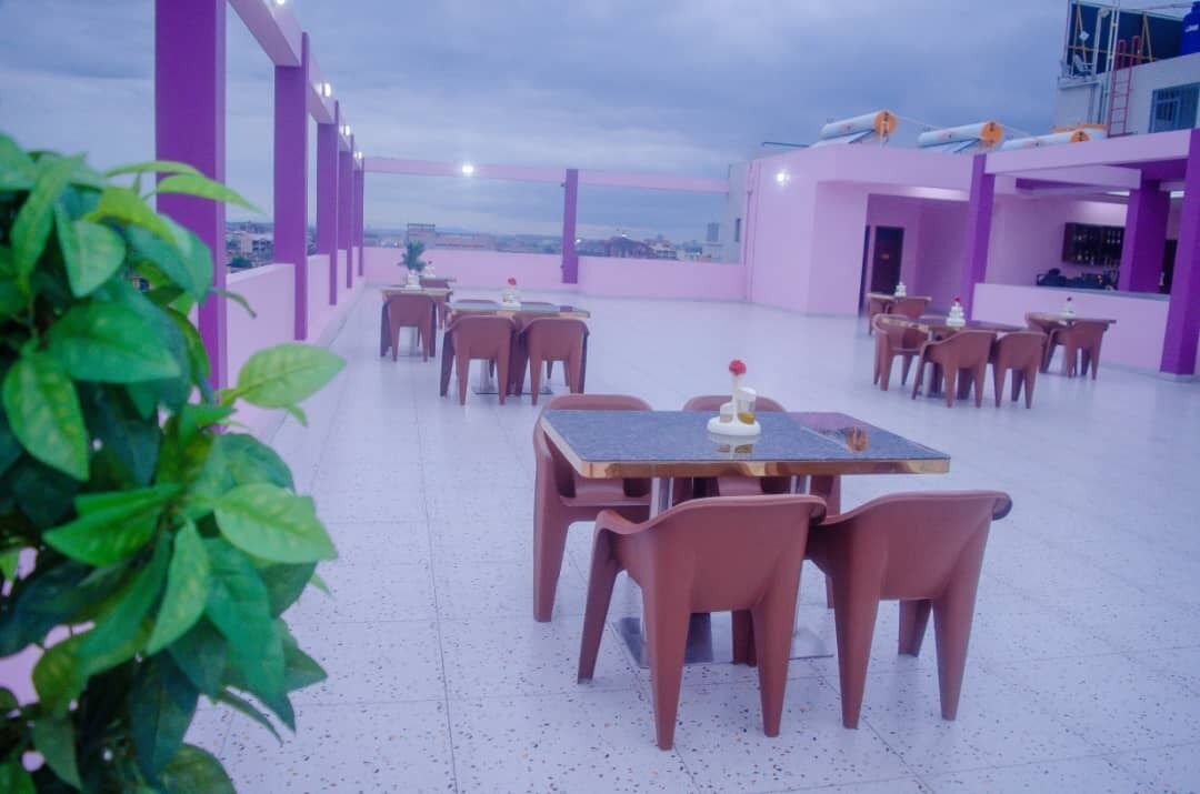 An outdoor dining area with tables and chairs, surrounded by purple walls and a view of the cityscape.