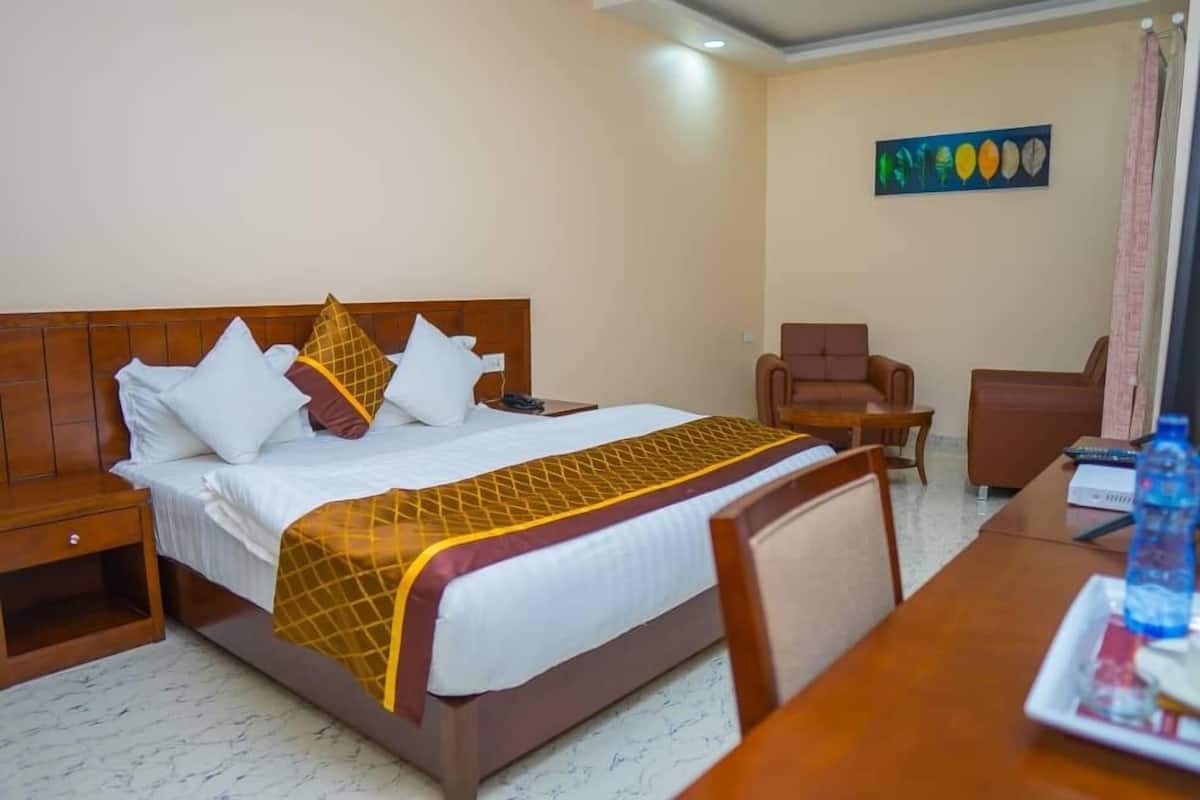 Habitación de hotel con cama, mesita de noche de madera, escritorio, silla y un cuadro en la pared.
