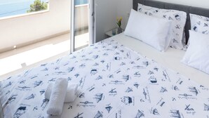 A bedroom with a bed, a nightstand, a wall-mounted light, and a view of the sea through a sliding door. - Dodjite i odmorite se u našem predivnom apartmanu (Marušići)