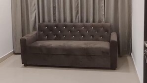 Une pièce avec un canapé gris, des rideaux beiges et un sol carrelé.