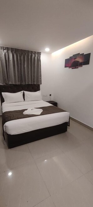 Een slaapkamer met een bed, nachtkastje, een wandlamp en een raam met gordijnen.