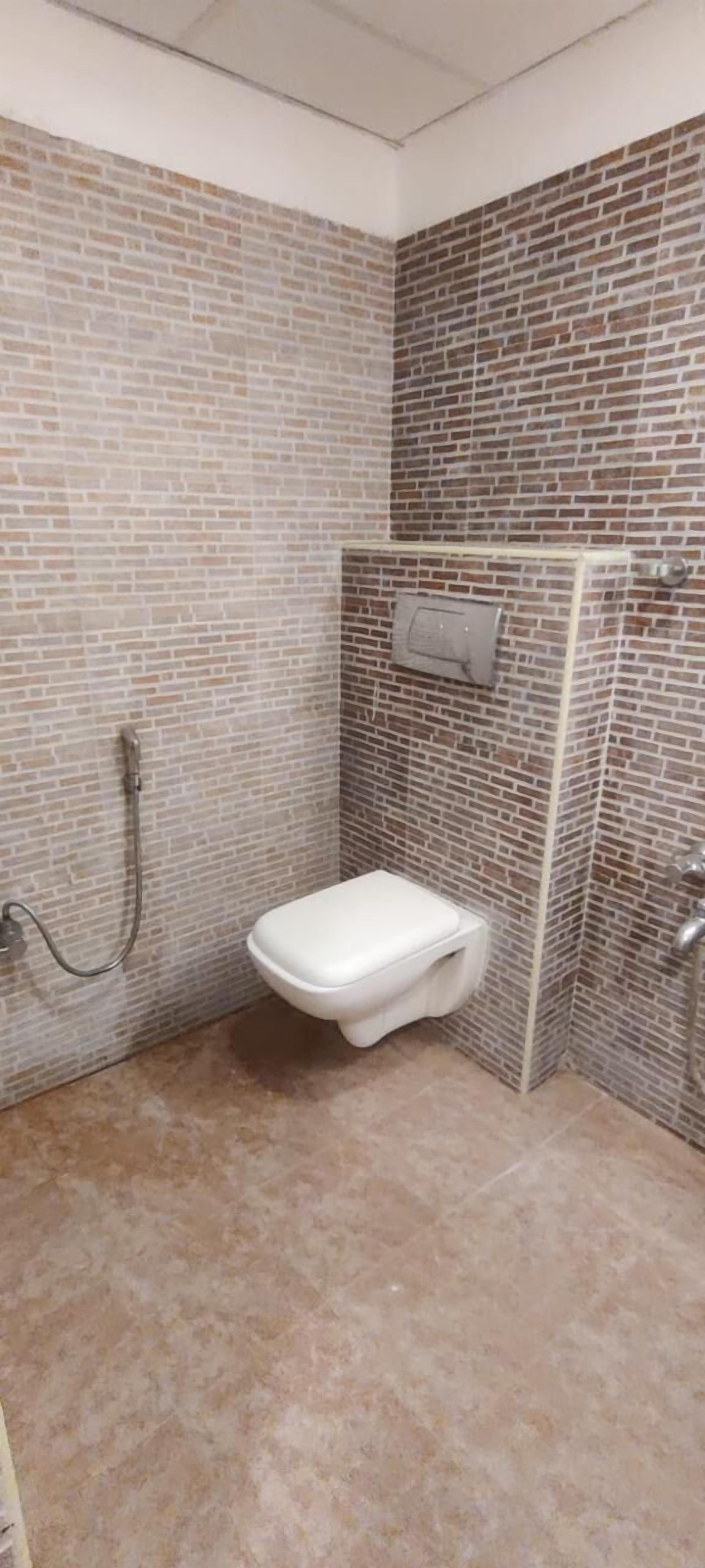 Un baño con inodoro blanco, zona de ducha y pared con azulejos.