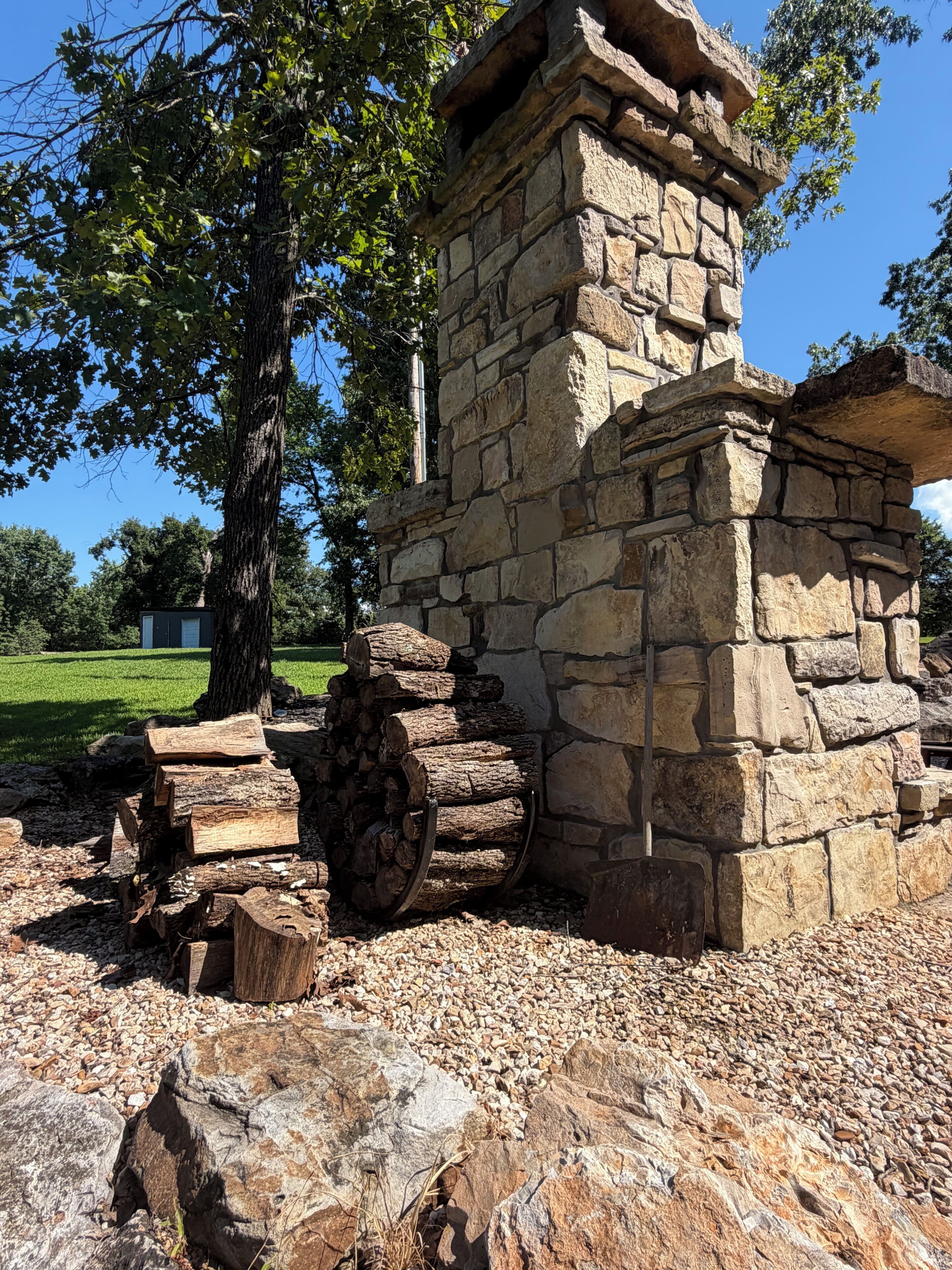 A stone structure with a chimney, surrounded by trees and a gravel area.