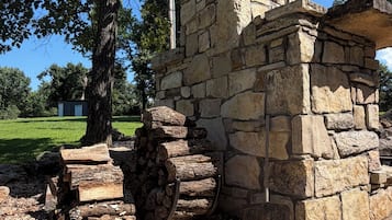 A stone structure with a chimney, surrounded by trees and a gravel area.