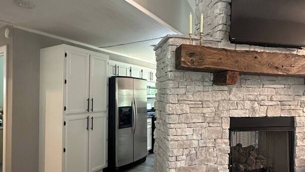 A modern kitchen with a stone fireplace, white cabinetry, and a flat-screen TV mounted above the fireplace. - Fireplace Lodge - 1 mile from Golf Course & 5 mins from the lake! (Isabella)