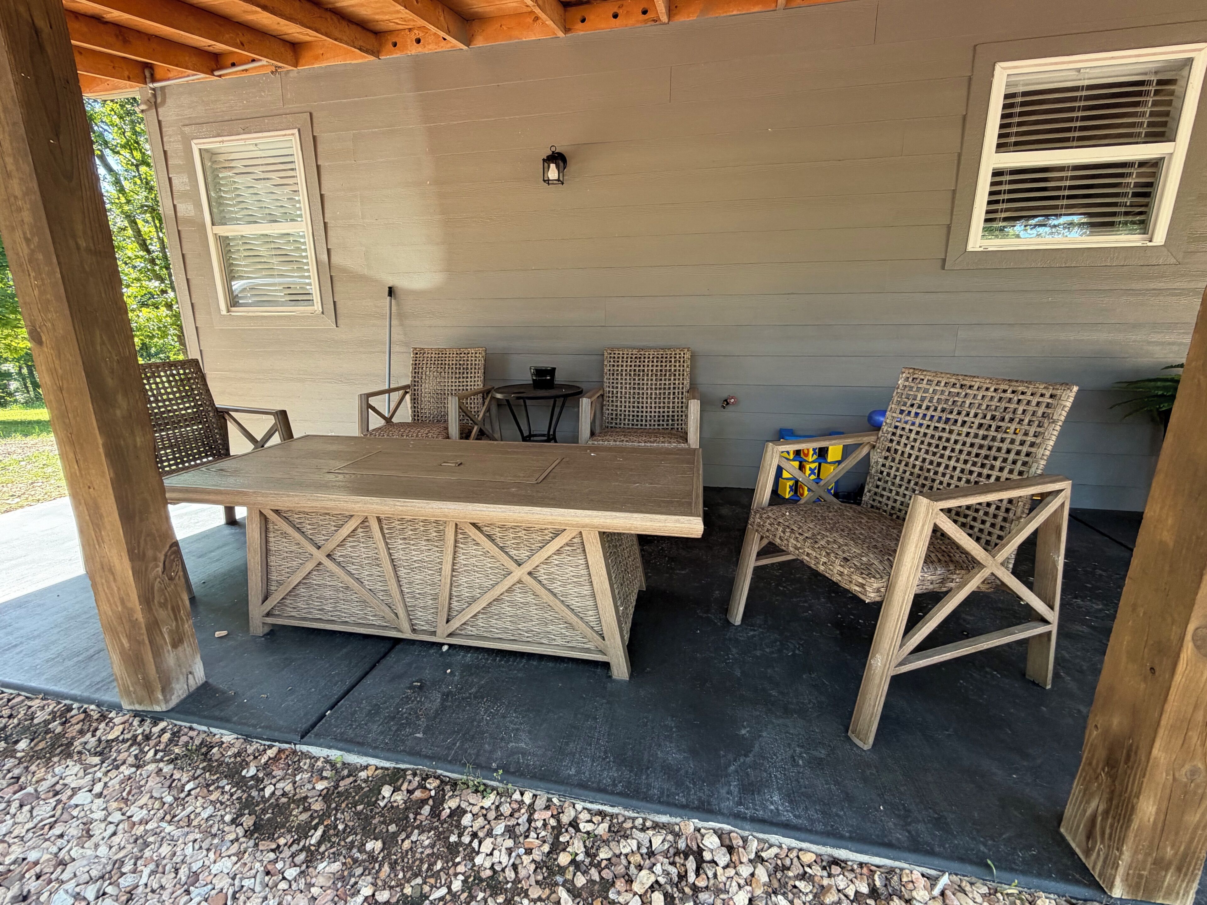 Ein überdachter Patio-Bereich mit einem Holztisch und vier Korbstühlen, einem kleinen runden Tisch sowie einer an der Wand befestigten Laterne.