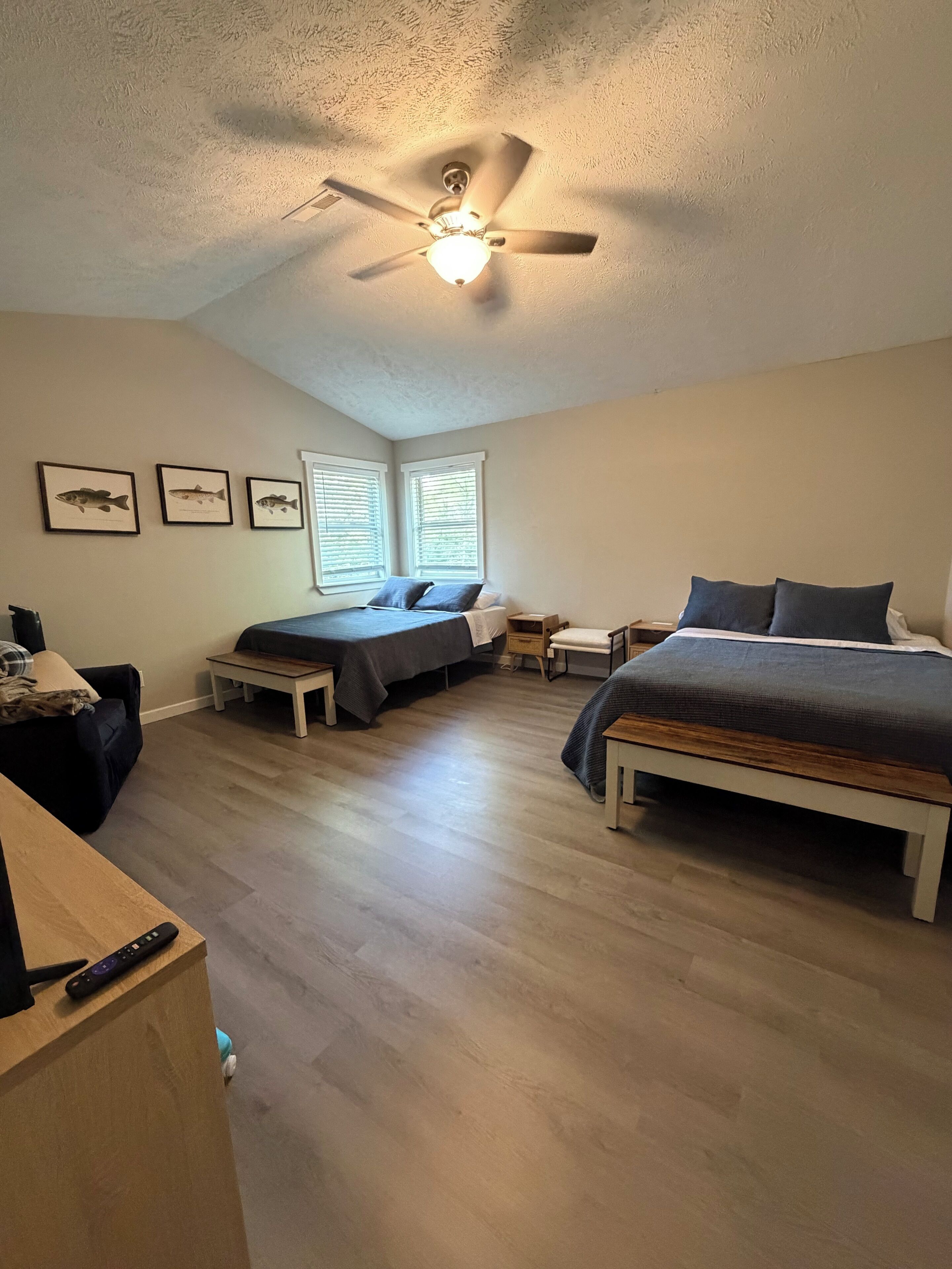 A bedroom with two beds, a ceiling fan, and framed fish pictures on the wall.