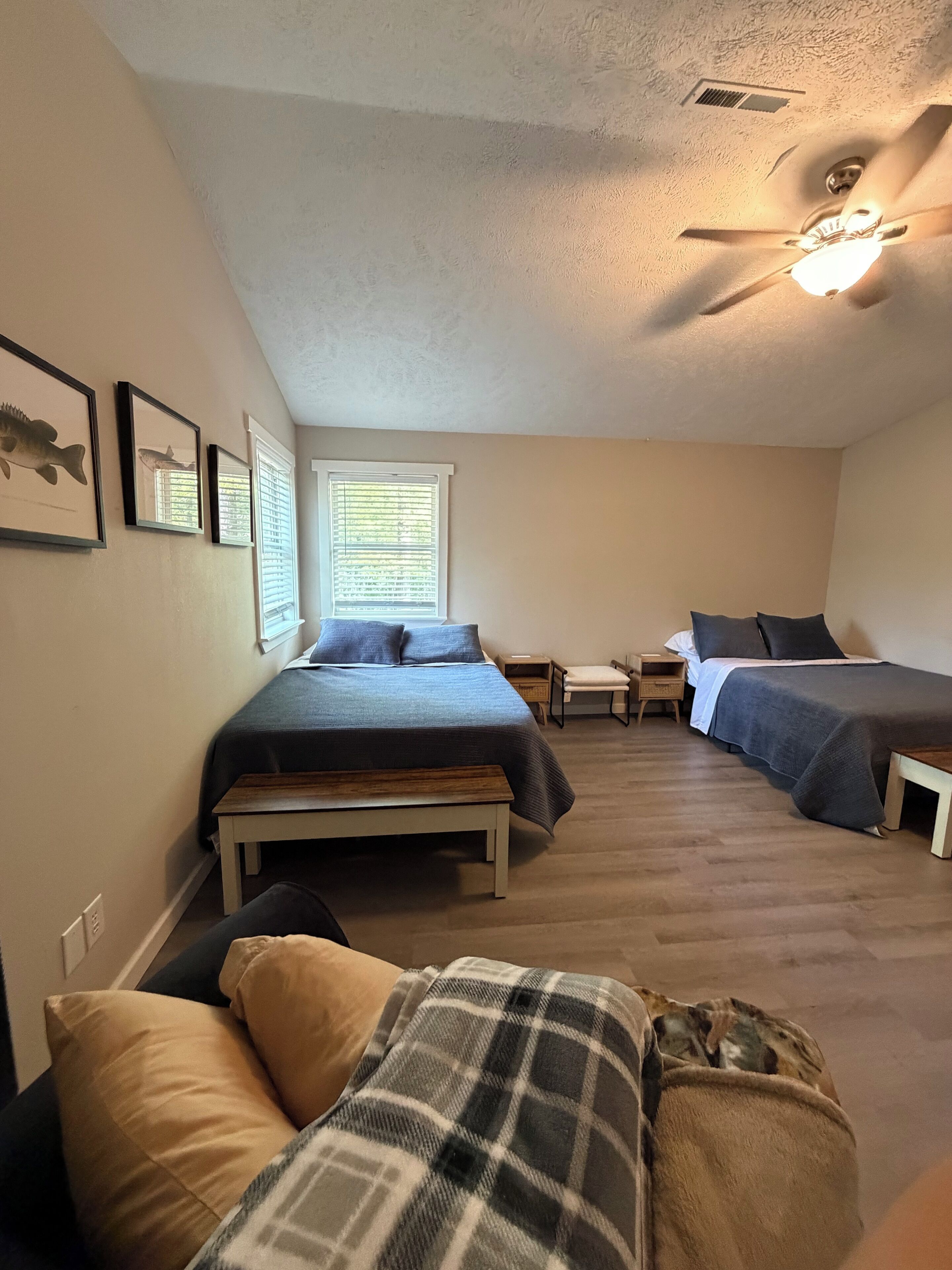 Ein Schlafzimmer mit einem Bett, zwei Nachttischen, einer Bank, einem Deckenventilator und einem Fenster mit Jalousien.