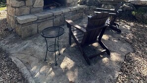 A stone-built outdoor fireplace with two Adirondack chairs and a small round table. - Fireplace Lodge - 1 mile from Golf Course & 5 mins from the lake! (Isabella)