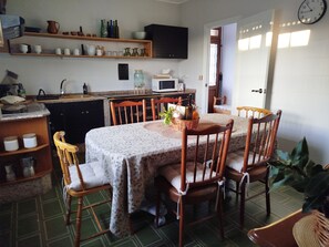 A dining area with a table set for four, surrounded by wooden chairs, a kitchen in the background, and a clock on the wall. - Casa Bandulu, cozy and comfortable house in a rural setting (Caldelas)